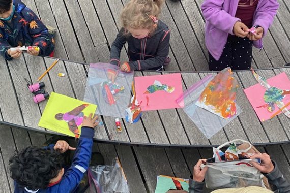 children kneeling around a low bench crafting birds with paper c/o Naval Cemetery Landscape