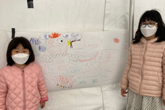 Two children in pink jackets posting with their bird art.