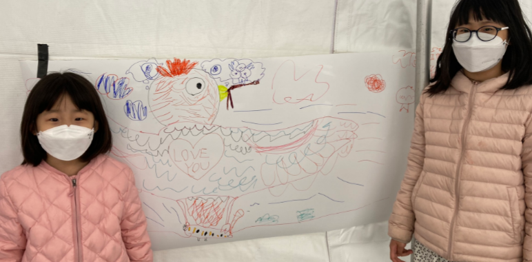 Two children in pink jackets posting with their bird art.