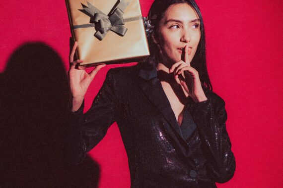 Person wearing a sparkly black jacket holding a wrapped gift.